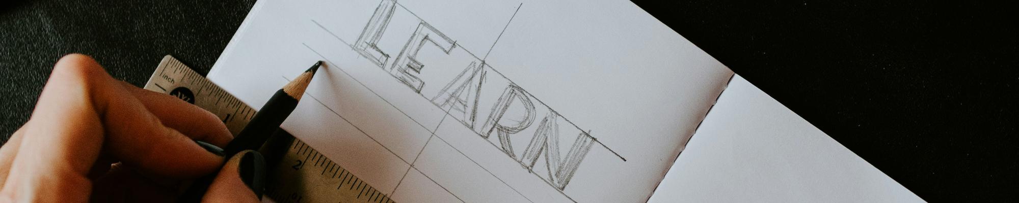 A person's hands against a note book where the word LEARN is written. 